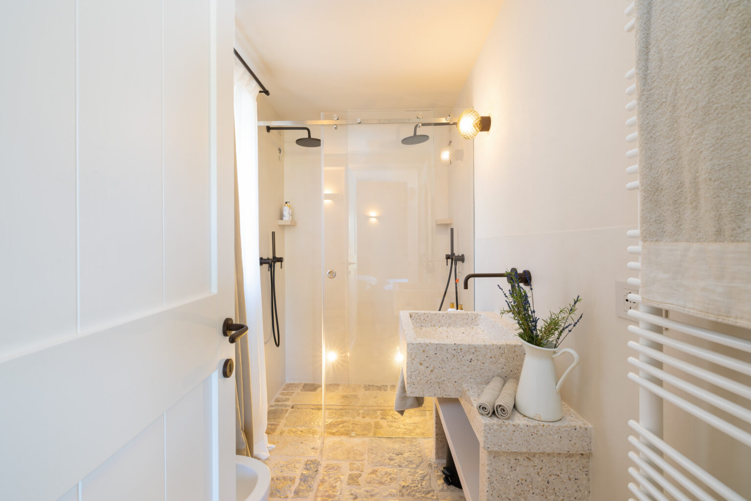 Modern bathroom interior featuring a glass shower, stone flooring, a minimalist sink, and stylish lighting fixtures. The design combines functionality with aesthetic appeal, showcasing neutral colors and natural materials for a serene atmosphere. | Only on SopranoVillas