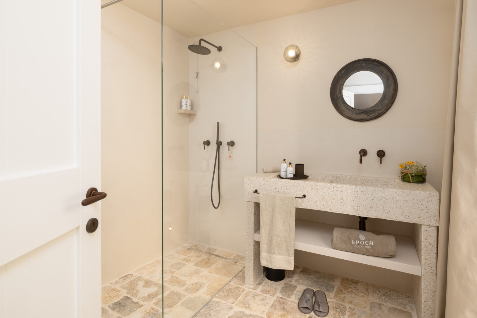 Modern bathroom featuring a glass shower, stone floor, and a minimalist vanity with natural stone sink, stylish fixtures, and decorative elements. | Only on SopranoVillas