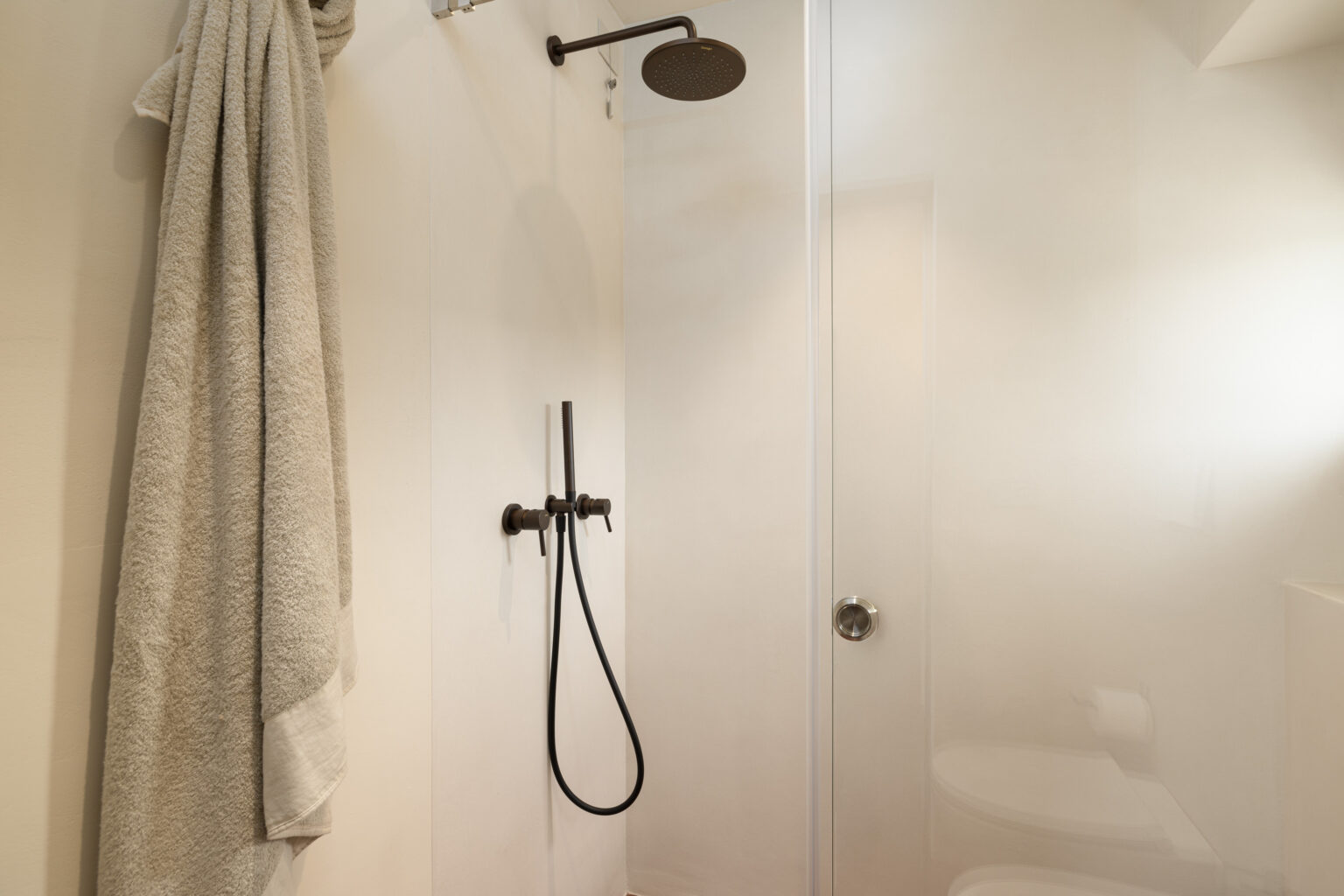 Modern bathroom shower featuring a sleek design, with a rainfall showerhead, a handheld shower attachment, and a plush towel hanging nearby. The glass shower enclosure and minimalist decor create a spacious and clean ambiance. | Only on SopranoVillas