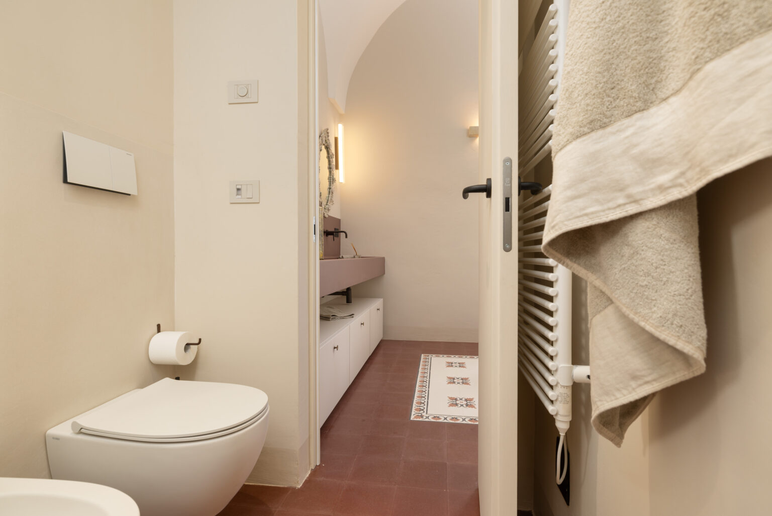 Modern bathroom interior featuring a sleek toilet, towel rack, and decorative floor tiles. The space is illuminated with soft lighting, showcasing a minimalist design and neutral color palette. | Only on SopranoVillas