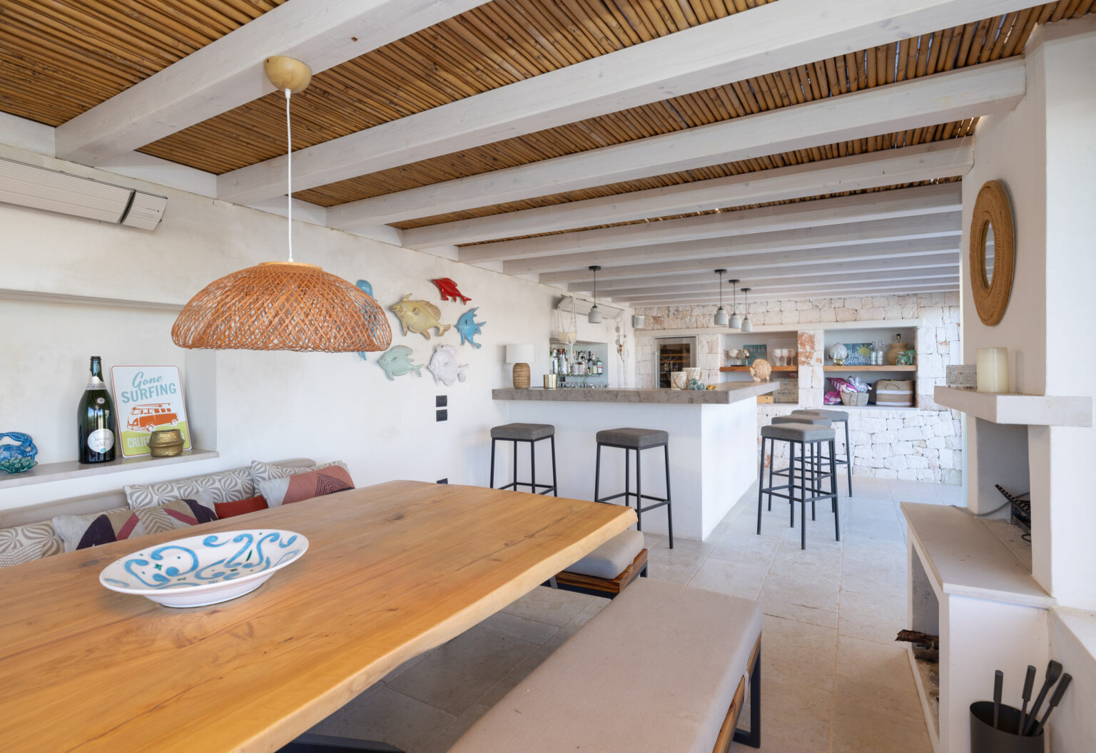 Modern open-concept kitchen and dining area featuring a wooden table, stylish bar stools, and a decorative pendant light, with a bright, airy atmosphere enhanced by natural light and coastal decor. | Only on SopranoVillas