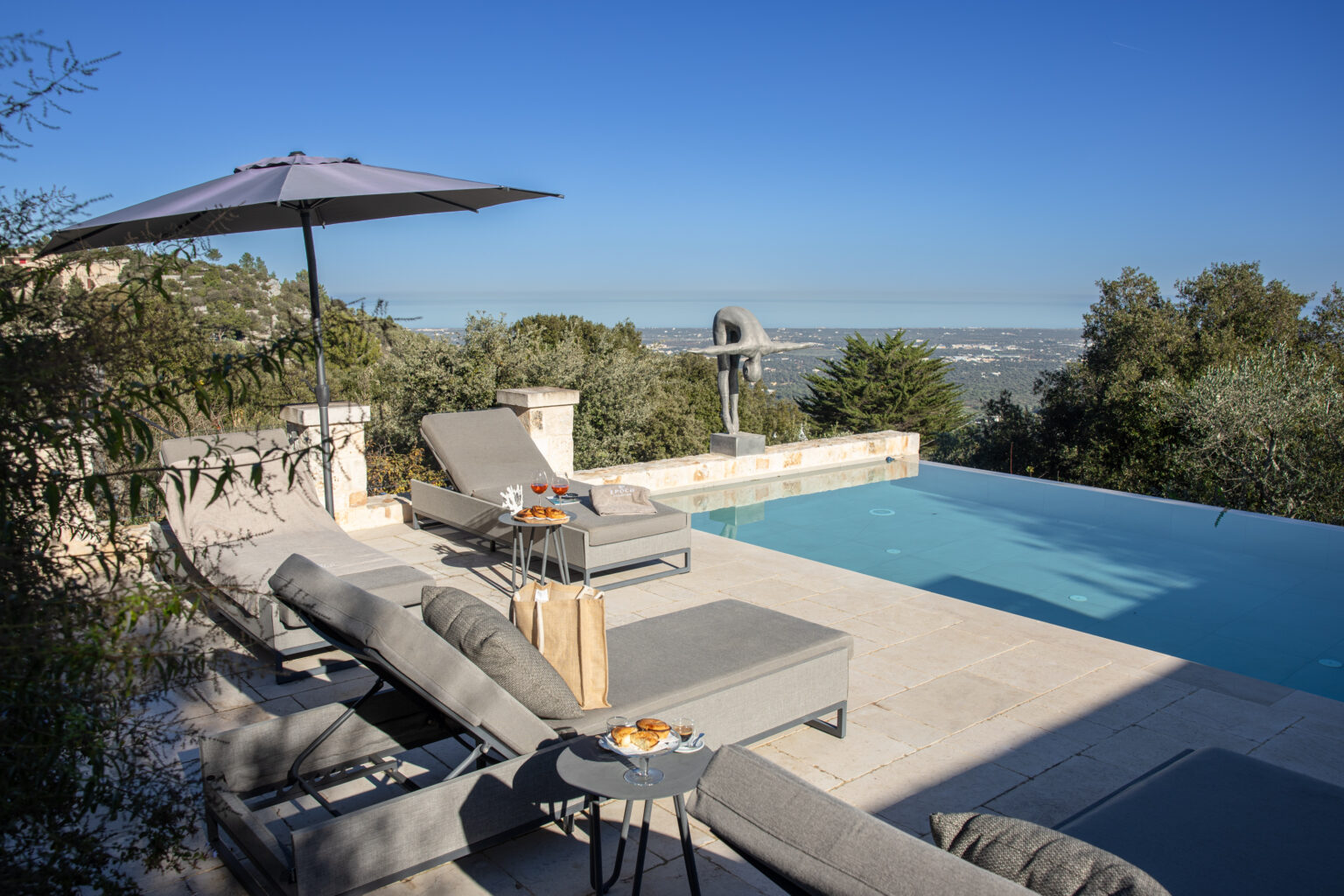Luxurious outdoor pool area with modern lounge chairs and an umbrella, offering a scenic view of the landscape. Ideal for relaxation and leisure. | Only on SopranoVillas