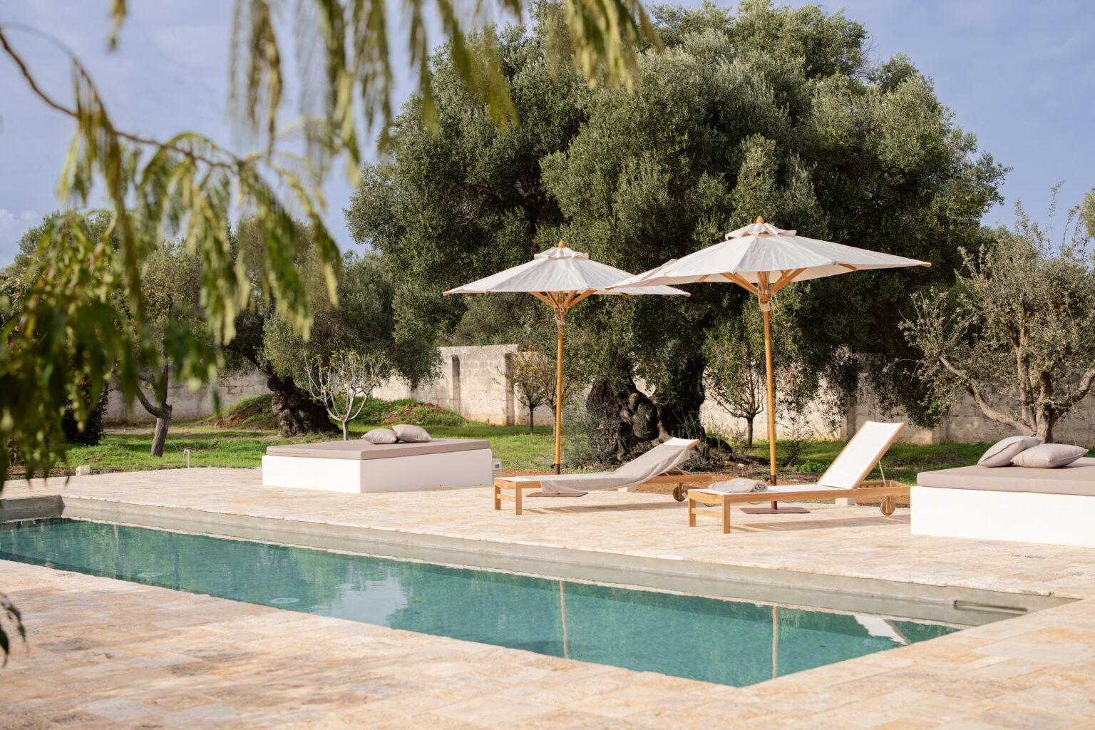 Luxurious outdoor pool area featuring comfortable loungers and elegant umbrellas, surrounded by olive trees and a serene landscape, perfect for relaxation and leisure. | Only on SopranoVillas