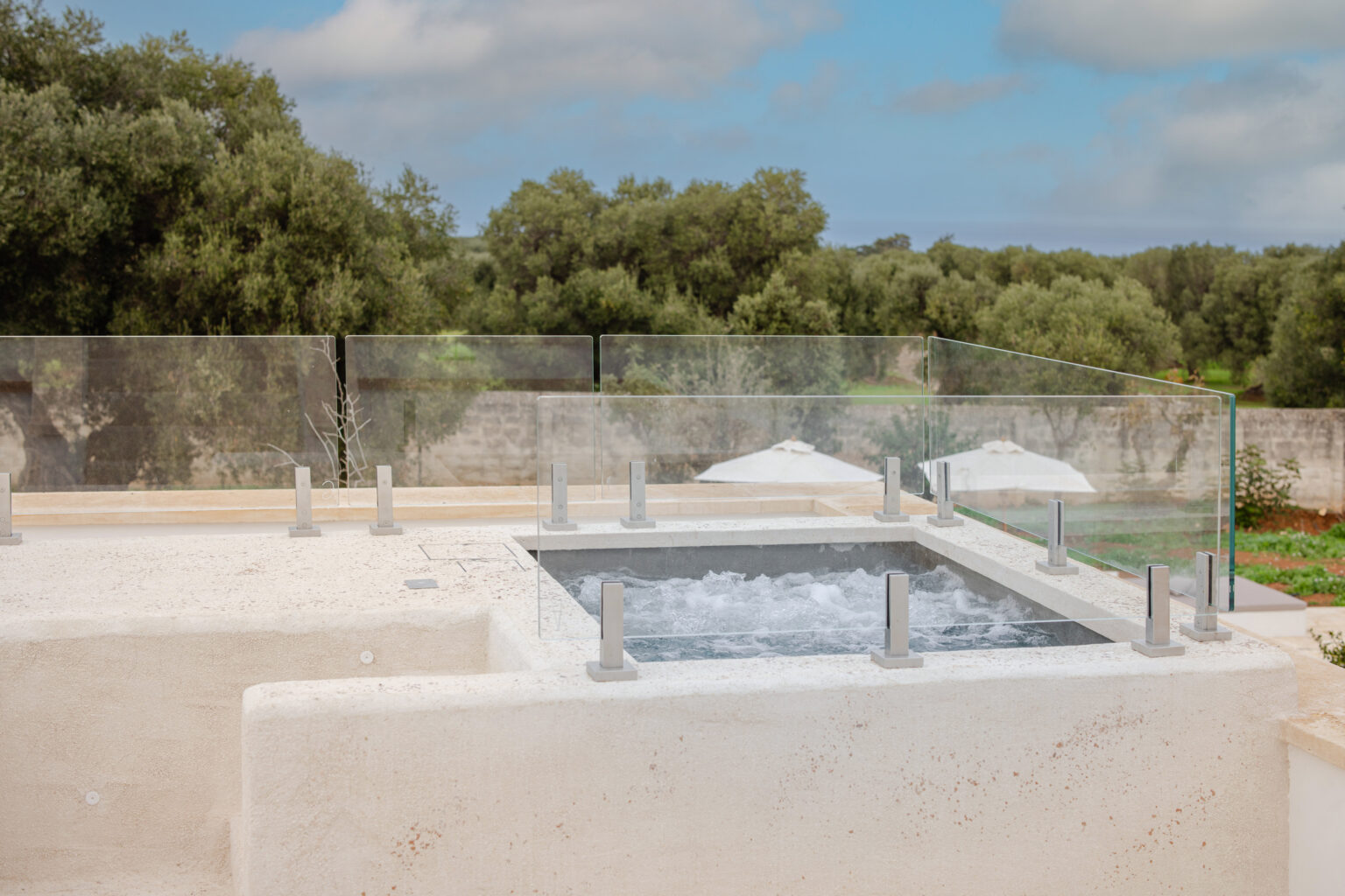 Modern rooftop hot tub surrounded by glass railing, set against a backdrop of lush greenery and blue skies. Ideal for relaxation and outdoor enjoyment. | Only on SopranoVillas