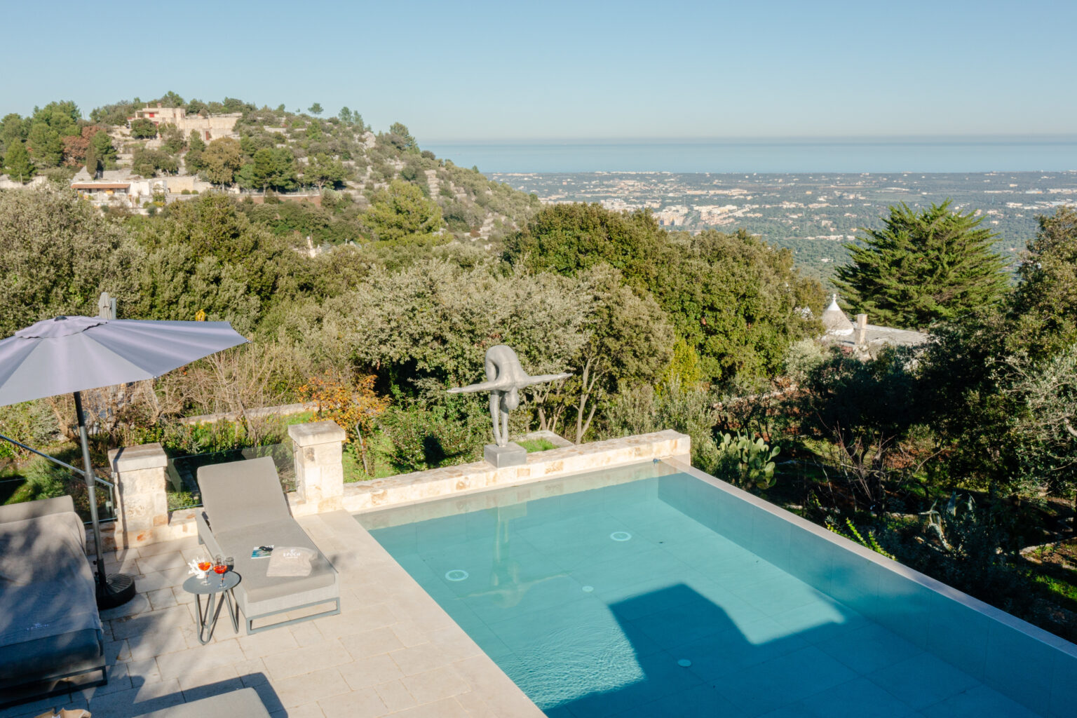Luxury villa with a swimming pool overlooking a scenic hillside and distant ocean view, surrounded by lush greenery and outdoor seating area. | Only on SopranoVillas