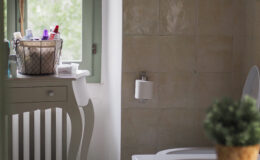 Bright and airy bathroom featuring a bathtub, a stylish white vanity with storage baskets, and a cozy green rug. Natural light streams through a large window, illuminating the space adorned with toiletries and a small potted plant.