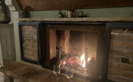 Cozy fireplace with a glowing fire, surrounded by rustic brick and a wooden mantel, featuring two wine glasses on the stone hearth, creating a warm and inviting atmosphere.
