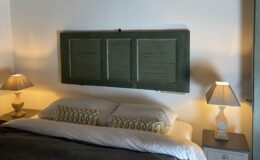 Cozy bedroom featuring a green wooden headboard, two bedside lamps with warm lighting, and decorative pillows on a neatly made bed. The walls are painted white, enhancing the room's bright and inviting atmosphere.
