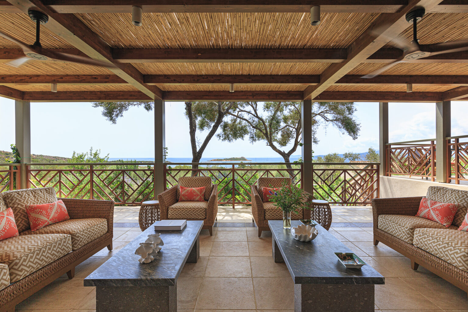 Cozy outdoor living area with wicker furniture, featuring patterned cushions and a stone coffee table, overlooking a scenic view of greenery and the ocean. Ideal for relaxation and entertaining in a tranquil setting. | Only on SopranoVillas
