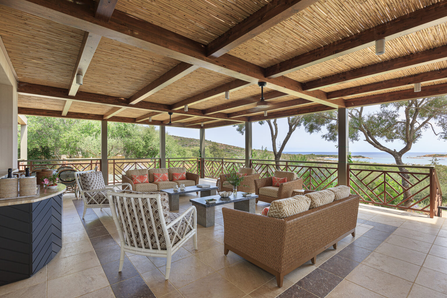 Spacious outdoor living area featuring comfortable wicker furniture, a coffee table, and decorative cushions, with a scenic view of greenery and the ocean in the background. The patio is covered by a bamboo ceiling, enhancing the relaxing atmosphere. Ideal for entertaining or enjoying nature. | Only on SopranoVillas