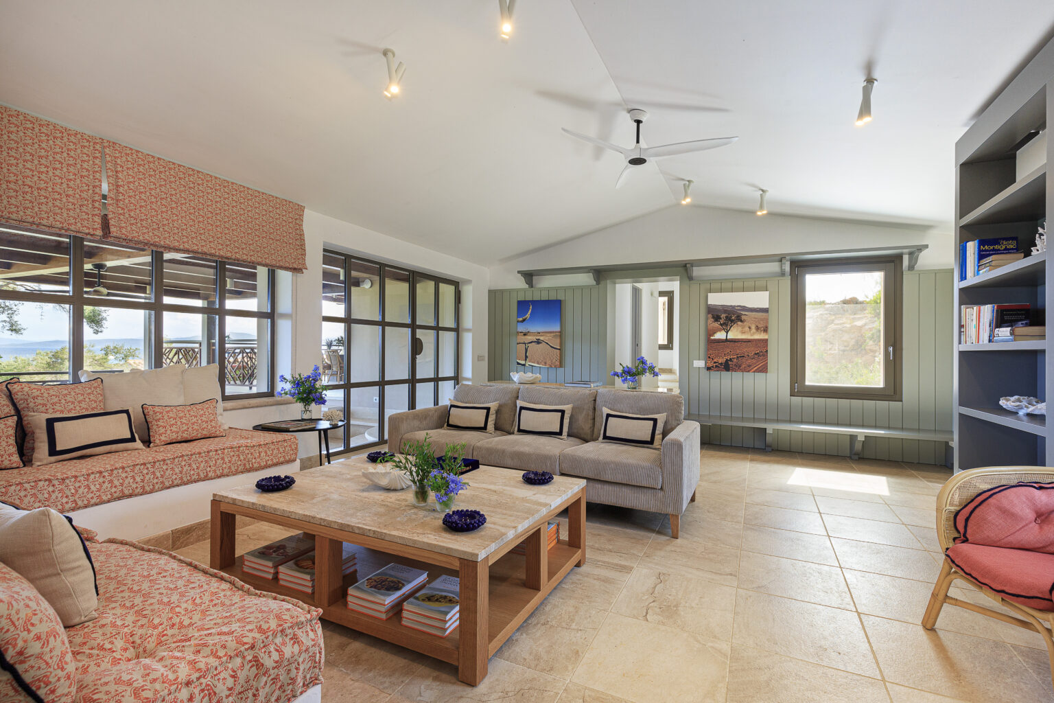Stylish living room featuring comfortable seating with patterned cushions, a wooden coffee table adorned with decorative plants, and large windows that offer scenic views. The space is enhanced by natural light and modern decor elements, creating a cozy and inviting atmosphere. | Only on SopranoVillas