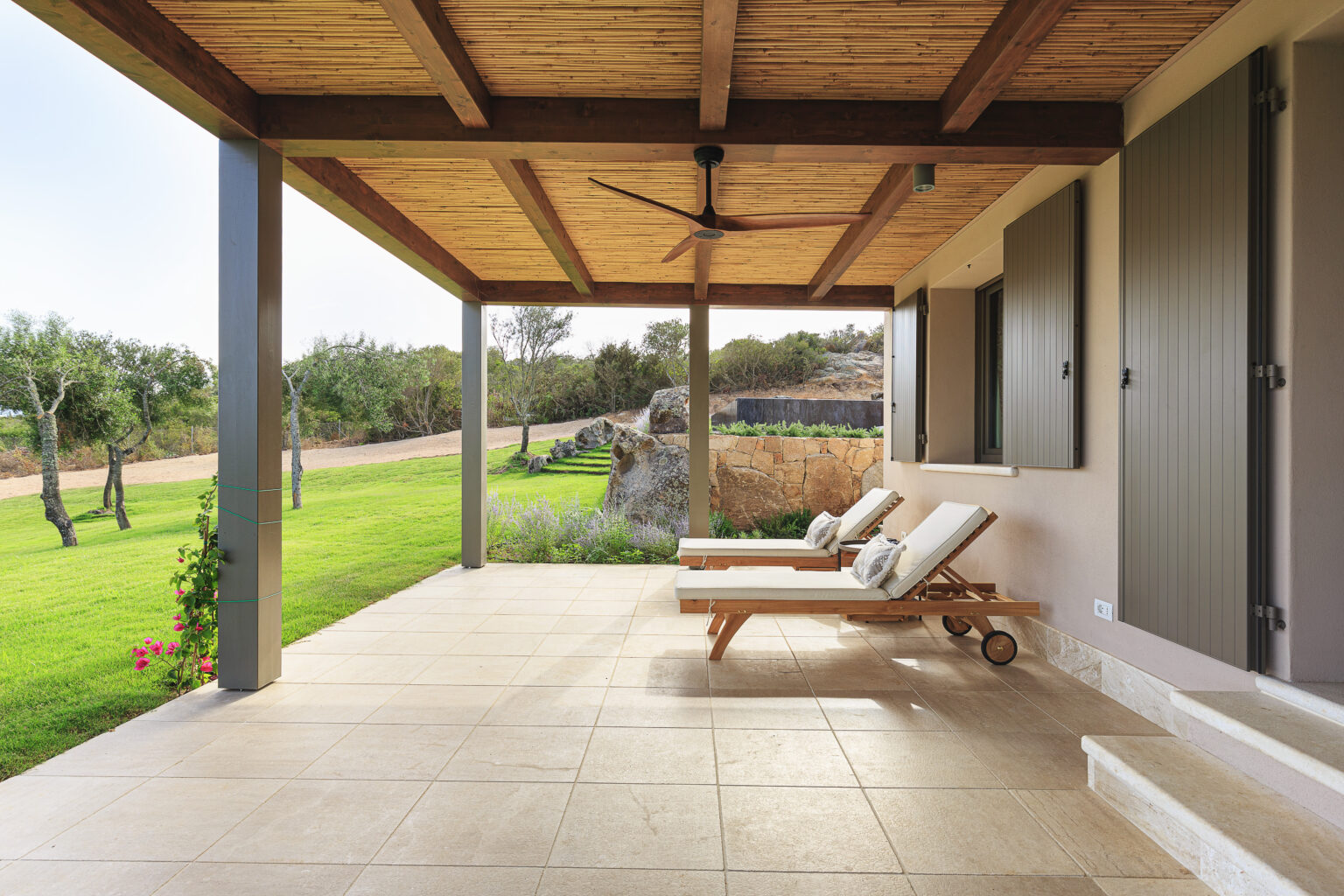 Modern patio featuring two reclining lounge chairs, a wooden ceiling, and views of a lush green landscape, ideal for outdoor relaxation and leisure. | Only on SopranoVillas
