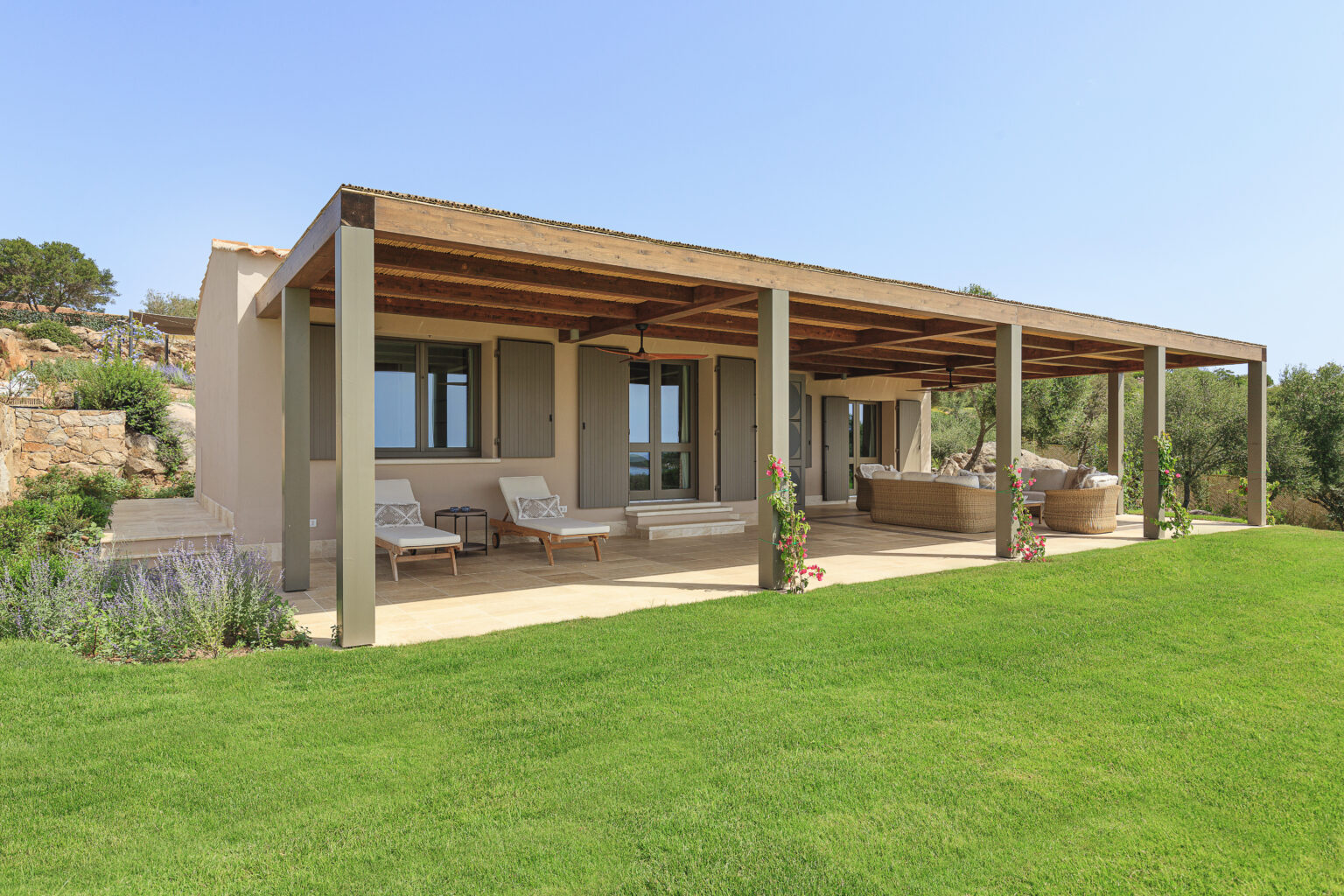 Modern villa with a spacious patio, featuring comfortable seating and lush green lawn, surrounded by natural landscape and blue sky. Ideal for outdoor relaxation and entertaining. | Only on SopranoVillas