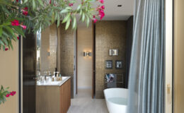 Modern bathroom design featuring a freestanding bathtub, dual vanity with sleek fixtures, and elegant decor. The space is illuminated by warm lighting, with a view framed by lush greenery and vibrant pink flowers.