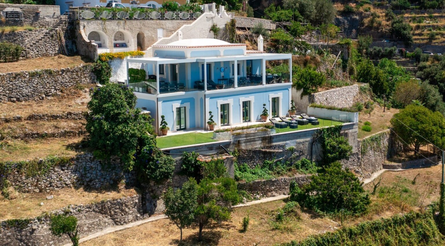 Modern hillside villa with expansive terraces and lush landscaping, overlooking scenic views. Ideal for luxury living and outdoor entertaining. | Only on SopranoVillas