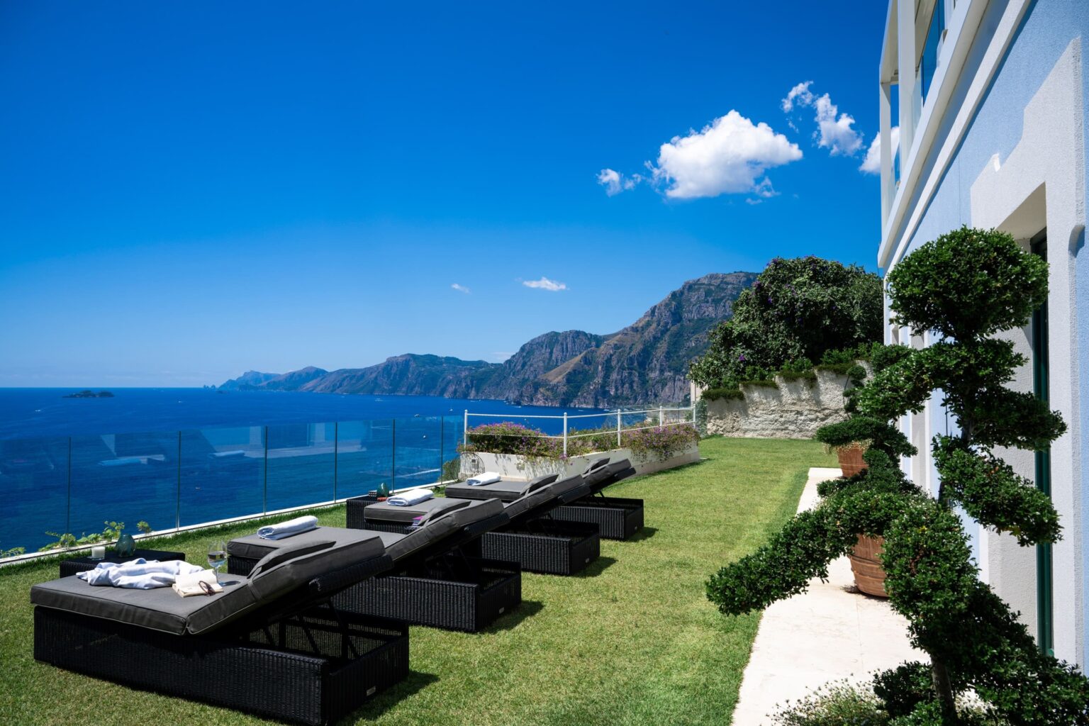 Luxury villa with sun loungers overlooking the stunning coastline of Italy, featuring lush greenery and breathtaking sea views, perfect for a relaxing getaway. | Only on SopranoVillas