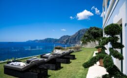 Luxury villa with sun loungers overlooking the stunning coastline of Italy, featuring lush greenery and breathtaking sea views, perfect for a relaxing getaway.