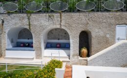 Cozy outdoor seating areas with white stone walls and colorful cushions, surrounded by lush greenery and decorative planters, ideal for relaxation in a Mediterranean-style garden.