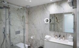 Modern bathroom interior featuring elegant marble walls, a glass shower enclosure, a sleek vanity with toiletries, and bright lighting for a stylish and functional design.