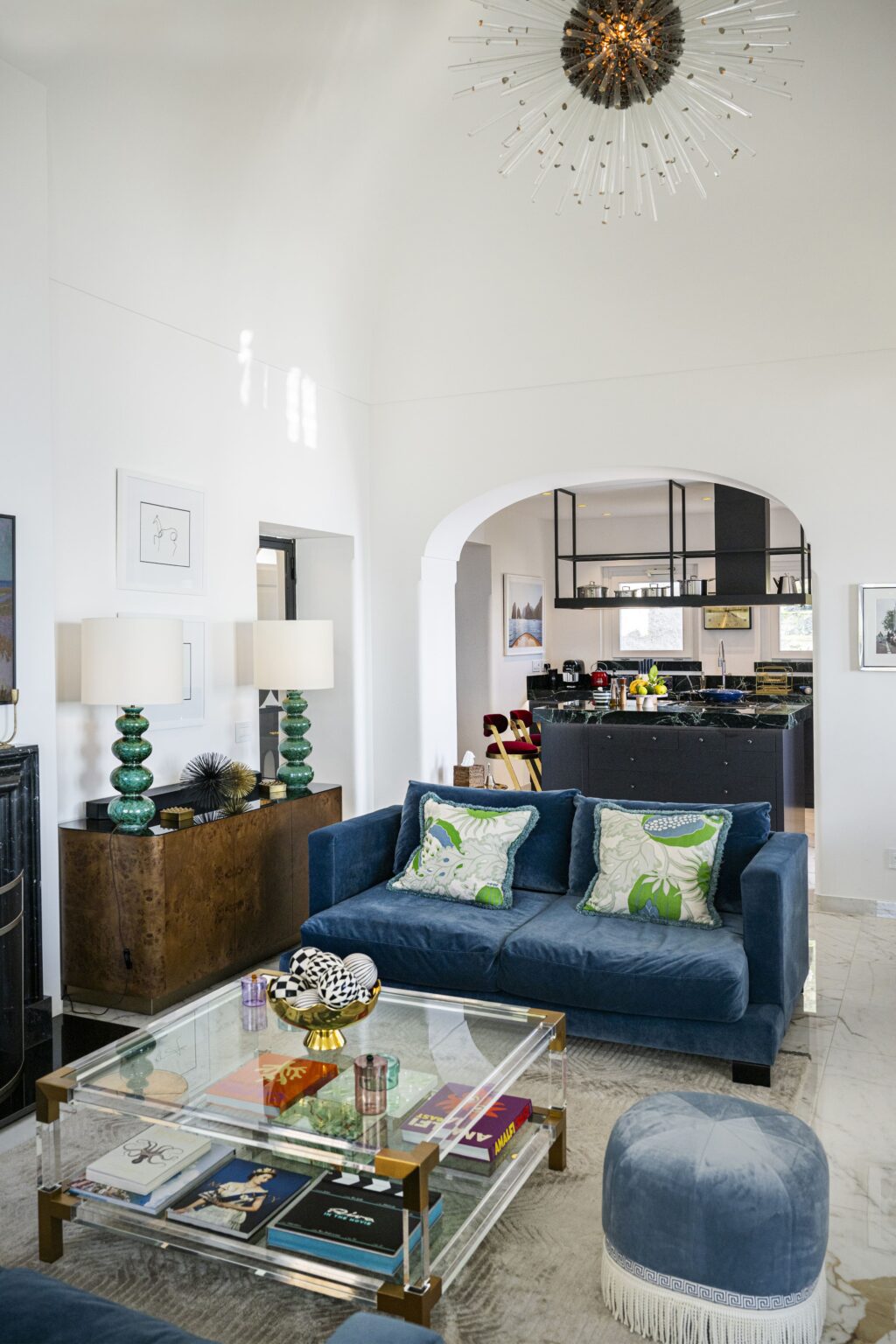 Elegant interior of a luxury villa in Italy featuring a stylish blue sofa, decorative pillows, and modern lighting, showcasing an open layout that connects the living area to a sophisticated kitchen. Ideal for upscale vacation rentals. | Only on SopranoVillas
