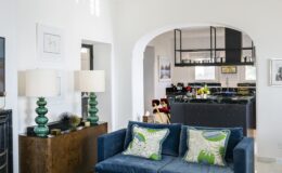 Elegant interior of a luxury villa in Italy featuring a stylish blue sofa, decorative pillows, and modern lighting, showcasing an open layout that connects the living area to a sophisticated kitchen. Ideal for upscale vacation rentals.