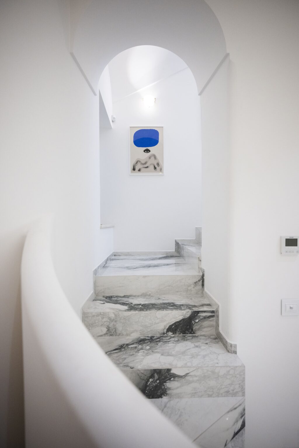 Elegant staircase leading to a luxury villa in Italy, featuring sleek marble steps and minimalist white walls, complemented by a unique artwork above. Ideal for showcasing high-end vacation rentals. | Only on SopranoVillas