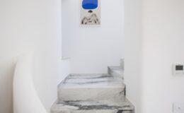 Elegant staircase leading to a luxury villa in Italy, featuring sleek marble steps and minimalist white walls, complemented by a unique artwork above. Ideal for showcasing high-end vacation rentals.