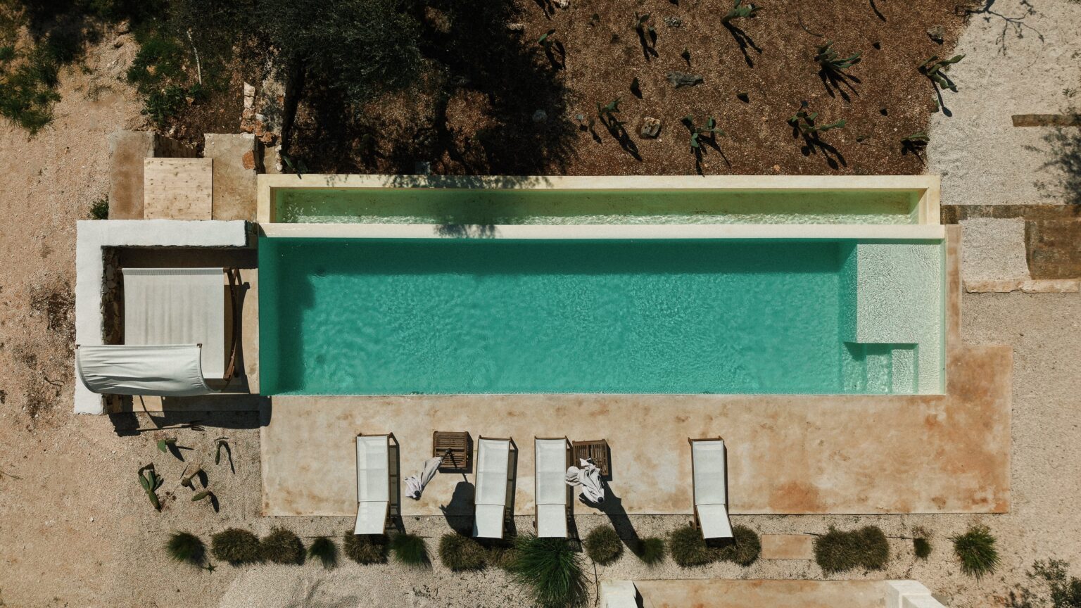 Aerial view of a modern swimming pool surrounded by lounge chairs and landscaped garden, featuring a turquoise water surface and minimalist design elements. | Only on SopranoVillas