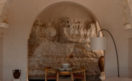 Modern interior design featuring a cozy seating area with curved sofas, a glass dining table, and a stylish floor lamp, set against a textured stone wall and arched ceiling. Ideal for showcasing contemporary home decor inspiration.