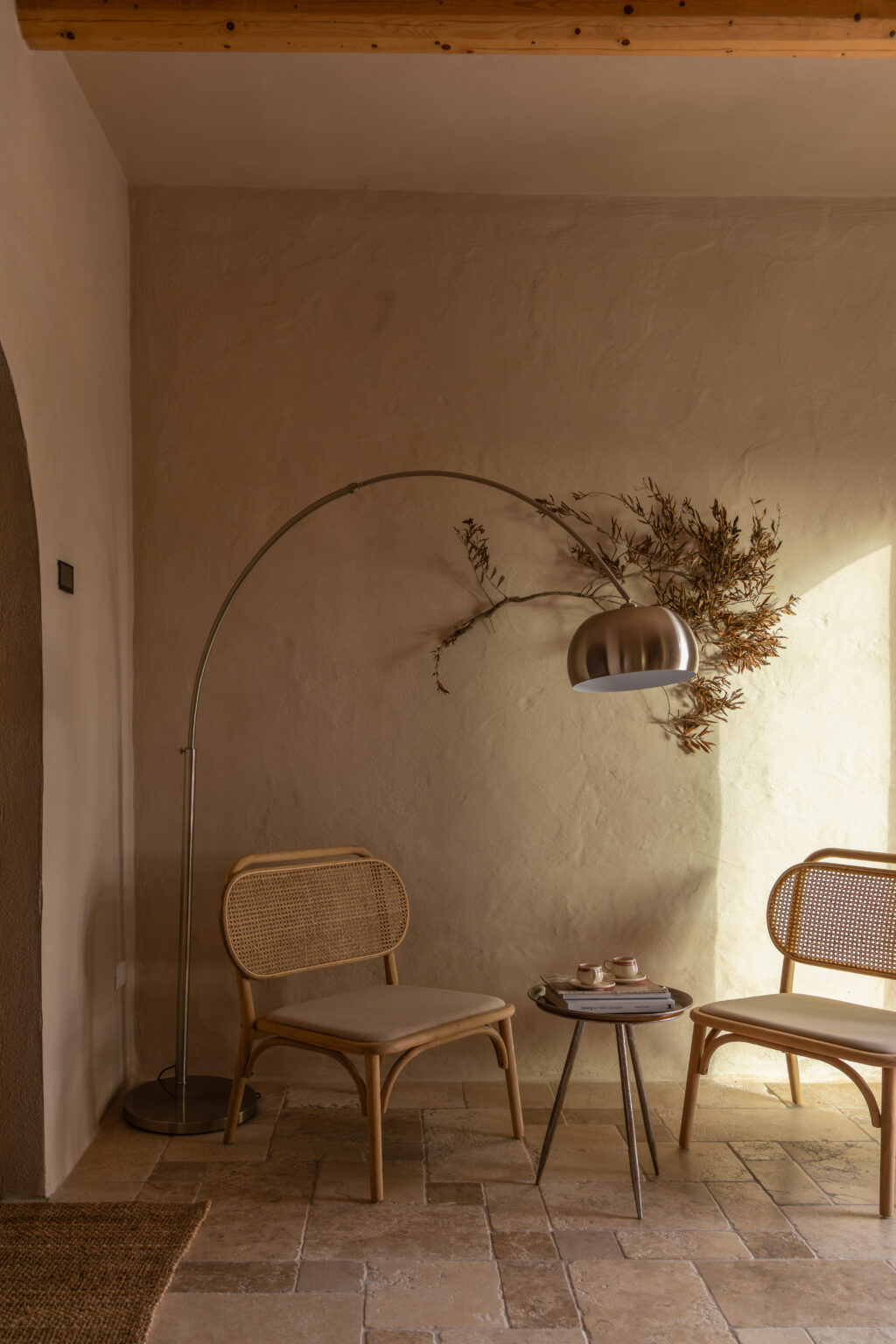 Cozy interior corner featuring two rattan chairs, a modern arc floor lamp, and a small round table with books and coffee cups, illuminated by natural light against a textured beige wall. | Only on SopranoVillas