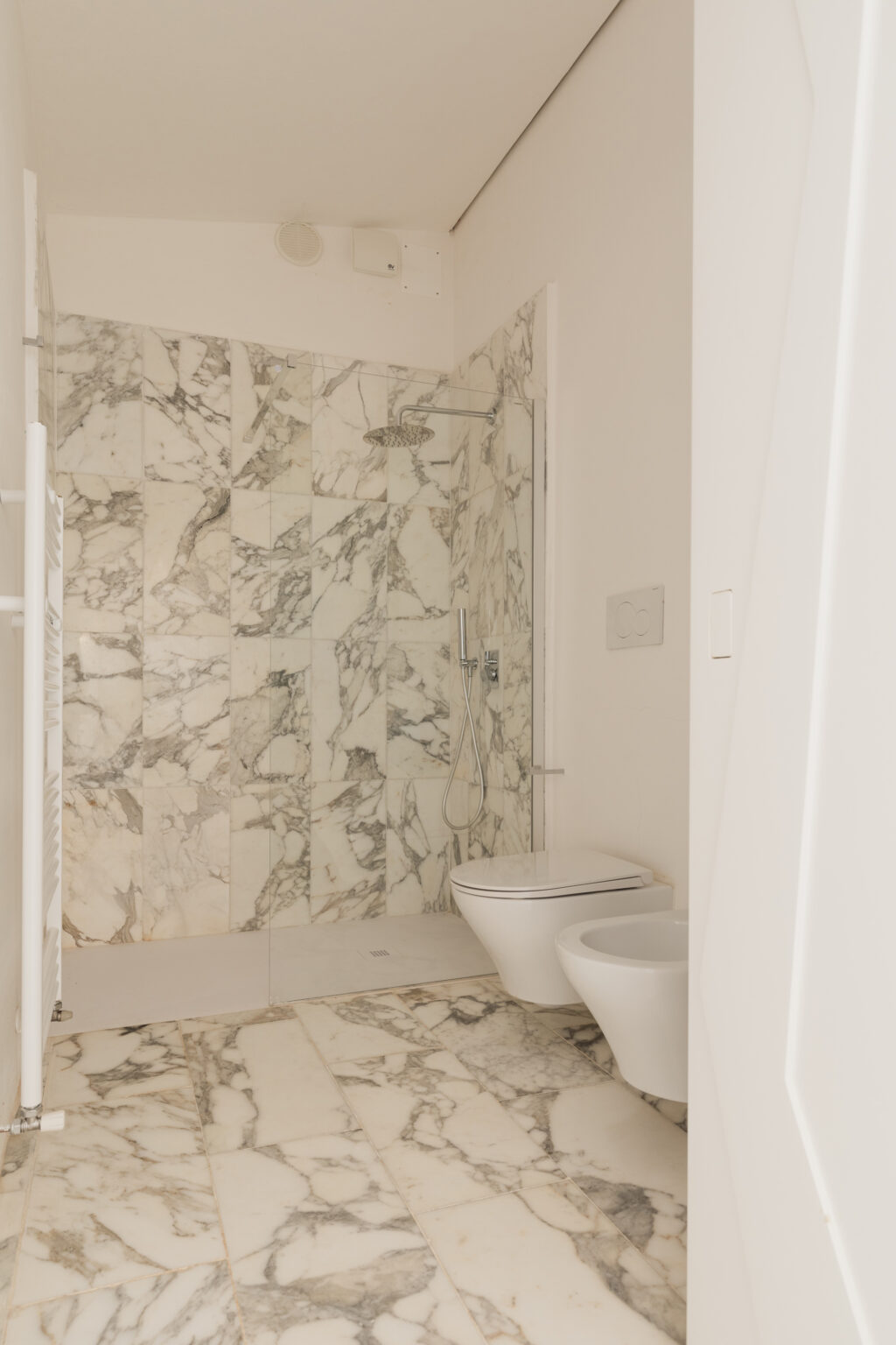 Modern bathroom featuring elegant marble walls and flooring, a glass shower with a rainfall showerhead, and a sleek toilet and bidet. The minimalist design emphasizes clean lines and a bright, airy atmosphere. | Only on SopranoVillas