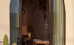 Modern arched doorway leading to a stylish interior with natural decor, featuring a small table and chairs, and a potted cactus outside. Soft curtains frame the entrance, highlighting the warm, inviting atmosphere.