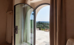 Interior view of a modern room featuring a large arched glass door opening to a scenic outdoor patio, with natural light illuminating the space and soft curtains framing the entrance, creating a serene atmosphere.
