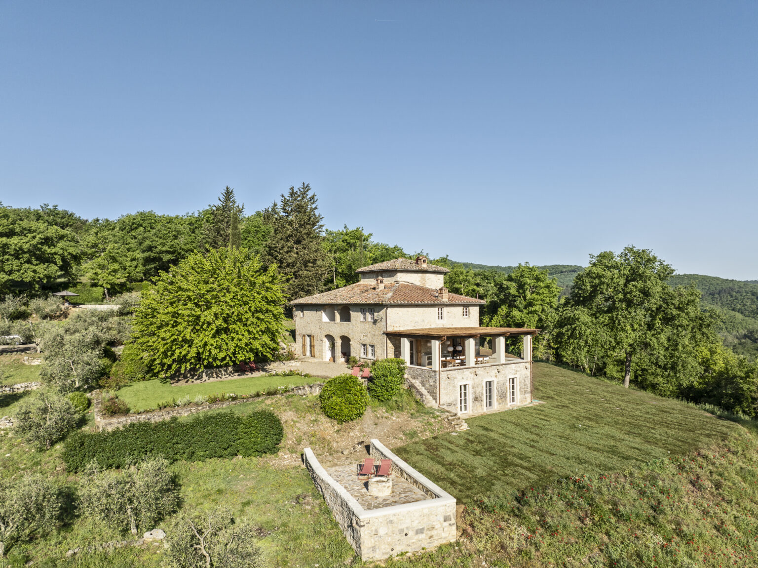 Aerial view of a charming stone villa surrounded by lush greenery and trees, featuring a spacious patio and well-maintained garden, set against a clear blue sky. Ideal for a tranquil retreat in nature. | Only on SopranoVillas