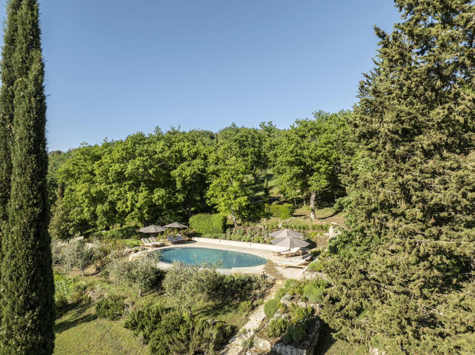 Serene outdoor swimming pool surrounded by lush greenery, featuring sun loungers and umbrellas, ideal for relaxation in a tranquil setting. Perfect for vacation rentals or luxury retreats. | Only on SopranoVillas
