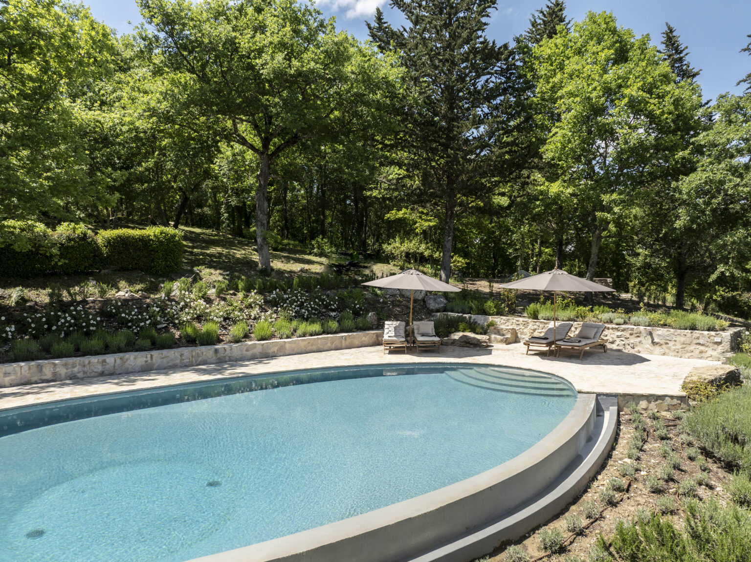 Serene outdoor swimming pool surrounded by lush greenery, featuring comfortable lounge chairs and umbrellas, ideal for relaxation in a tranquil garden setting. | Only on SopranoVillas