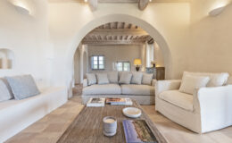Cozy and modern living room featuring a light-colored sofa, comfortable armchair, and a rustic wooden coffee table. The space is enhanced by arched doorways, soft lighting, and natural textures, creating a warm and inviting atmosphere. Perfect for interior design inspiration.