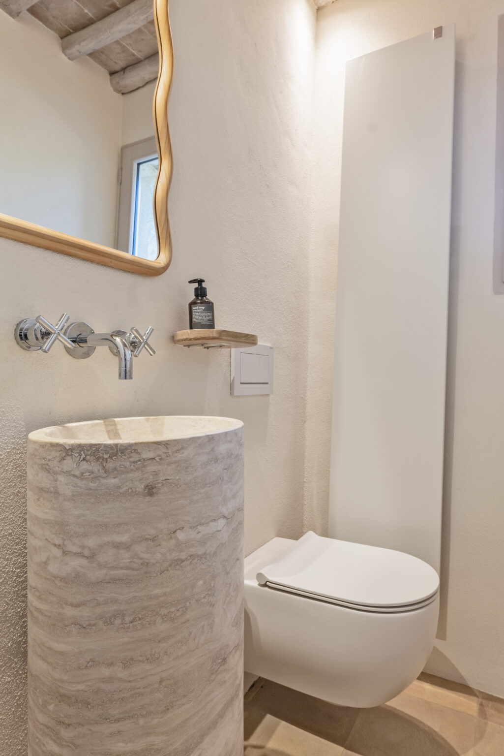 Modern bathroom design featuring a round marble sink, sleek white toilet, and a stylish wall-mounted mirror. The minimalist decor includes a wooden shelf with a soap dispenser, creating a clean and elegant atmosphere. | Only on SopranoVillas