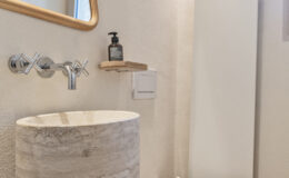 Modern bathroom design featuring a round marble sink, sleek white toilet, and a stylish wall-mounted mirror. The minimalist decor includes a wooden shelf with a soap dispenser, creating a clean and elegant atmosphere.