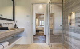 Modern bathroom interior featuring a stone sink, stylish mirror, and glass shower. The open doorway reveals a cozy bedroom with natural light and wooden flooring, enhancing the inviting atmosphere. Ideal for showcasing contemporary home design.