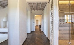 Modern interior hallway featuring a wooden herringbone floor, white walls, and a glass shower. The space is illuminated by natural light, showcasing a minimalist design with a cozy atmosphere.