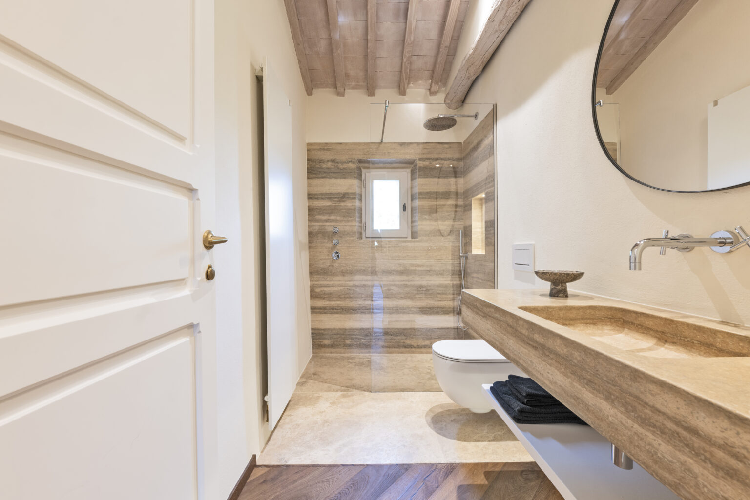 Modern bathroom design featuring a walk-in shower with glass enclosure, natural stone accents, a stylish sink with a wooden countertop, and elegant wooden flooring. | Only on SopranoVillas