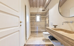 Modern bathroom design featuring a walk-in shower with glass enclosure, natural stone accents, a stylish sink with a wooden countertop, and elegant wooden flooring.
