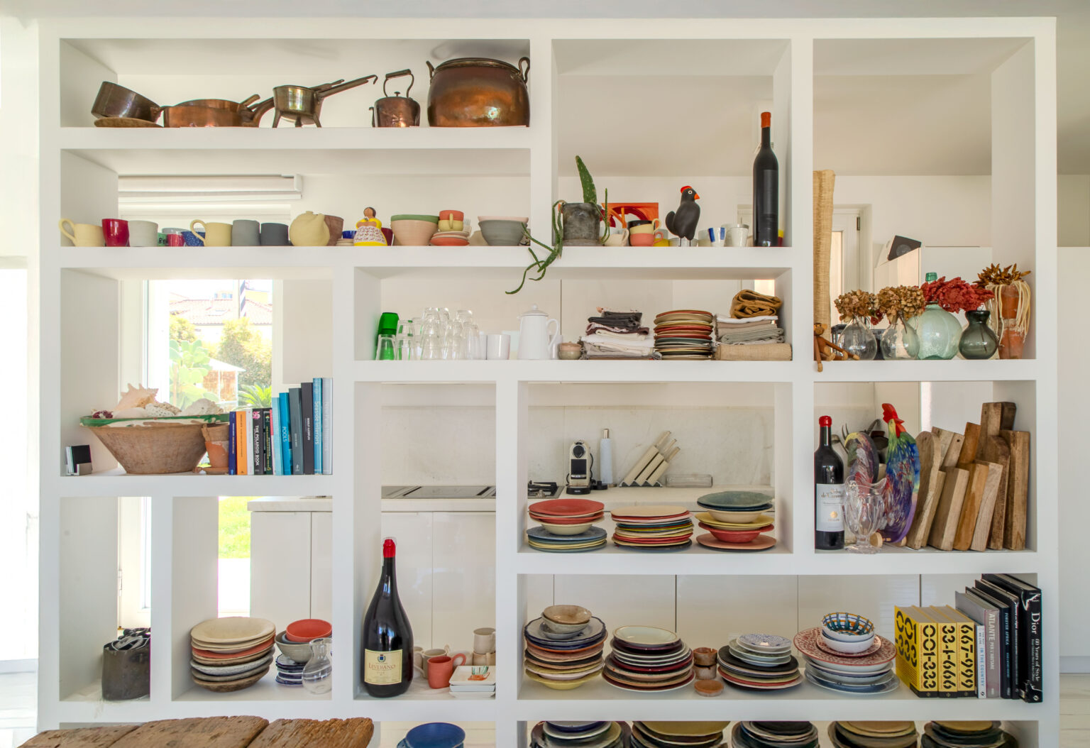 Modern kitchen shelving featuring an assortment of colorful plates, bowls, and cups, alongside decorative items like plants and books. The design emphasizes a clean, organized aesthetic with both functional kitchenware and artistic accents. | Only on SopranoVillas