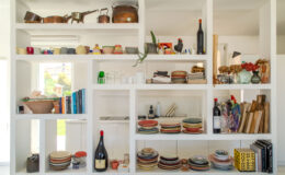 Modern kitchen shelving featuring an assortment of colorful plates, bowls, and cups, alongside decorative items like plants and books. The design emphasizes a clean, organized aesthetic with both functional kitchenware and artistic accents.