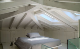 Bright and modern attic bedroom featuring a spacious bed with gray bedding, surrounded by minimalist storage cabinets and illuminated by skylights, showcasing clean lines and a contemporary design.