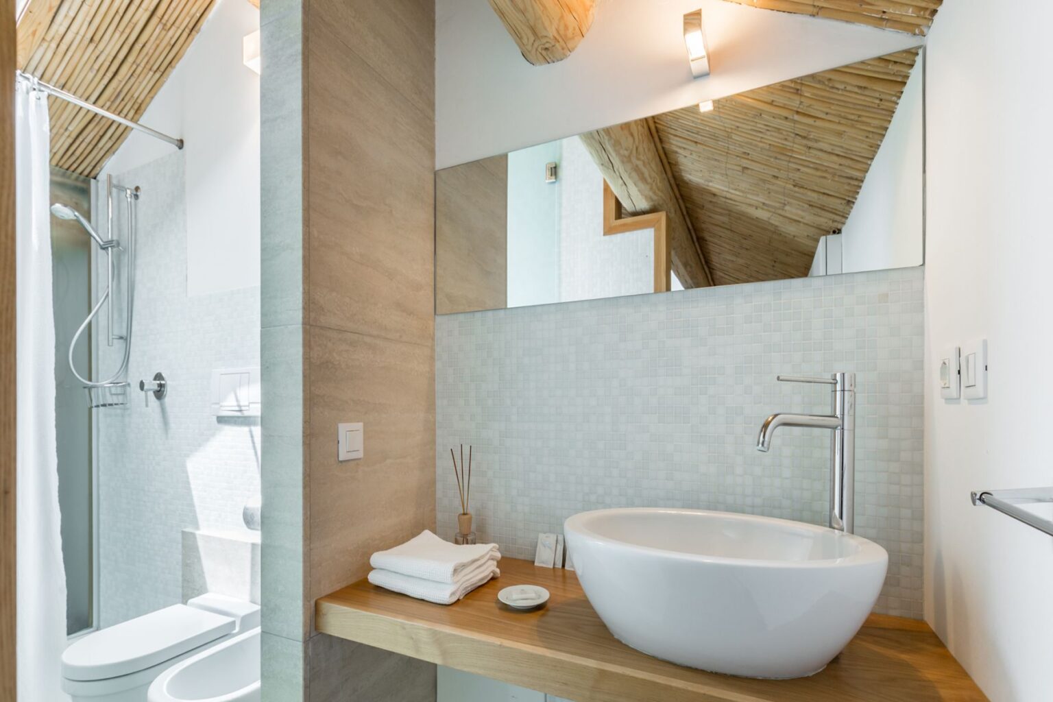 Modern bathroom featuring a stylish freestanding sink, wooden countertop, and elegant shower area with glass enclosure. The space is illuminated by natural light and complemented by a bamboo ceiling, creating a serene and contemporary atmosphere. | Only on SopranoVillas