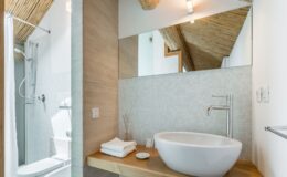 Modern bathroom featuring a stylish freestanding sink, wooden countertop, and elegant shower area with glass enclosure. The space is illuminated by natural light and complemented by a bamboo ceiling, creating a serene and contemporary atmosphere.