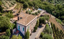 Aerial view of a charming countryside villa surrounded by olive trees and vineyards, featuring a swimming pool and landscaped gardens, showcasing a rustic stone pathway leading to the house.