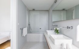 Modern bathroom design featuring a spacious layout with a glass shower, elegant marble walls, dual vessel sinks, and stylish chrome fixtures. The room is well-lit with natural light and includes decorative elements like fresh flowers and neatly arranged towels.
